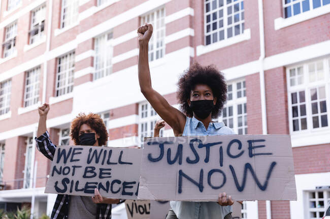 Протестующие мужчины и женщины маршируют в масках с плакатами протеста и поднимают кулаки. Демонстрация равных прав и справедливости во время ковида 19 пандемии коронавируса. . — стоковое фото