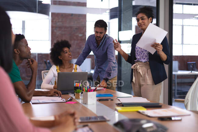 Diverse group of creative colleagues in discussion at work using laptop holding document. independent creative design business. — Stock Photo