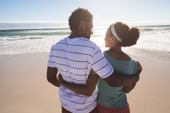 Feliz pareja afroamericana en la playa abrazando. tiempo de ocio al aire libre saludable junto al mar. - foto de stock