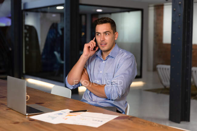 Porträt eines lässigen kaukasischen Geschäftsmannes, der am Schreibtisch auf dem Smartphone spricht. Geschäftsmann bei der Arbeit im modernen Büro. — Stockfoto