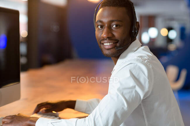 Портрет щасливого афроамериканського бізнесмена, який носить навушники телефону і дивиться на камеру. Бізнесмен на роботі в сучасному офісі.. — стокове фото