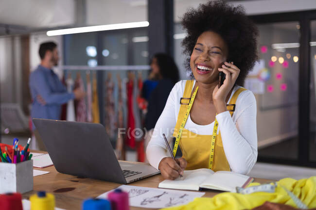 Stilista donna americana indossando metro sarto parlare da smartphone sorridente. attività indipendente di design creativo. — Foto stock