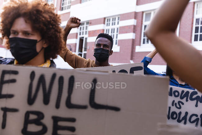 Divers manifestants masculins et féminins défilent masqués tenant des pancartes de protestation et levant les poings. Manifestation pour l'égalité des droits et la justice pendant la pandémie de coronavirus covid 19. . — Photo de stock