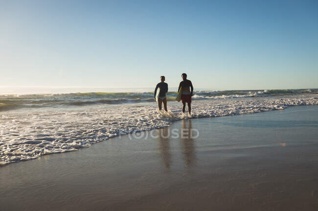 Glückliches afrikanisch-amerikanisches Paar mit Surfbrettern an der Küste. gesunde Freizeit im Freien am Meer. — Stockfoto