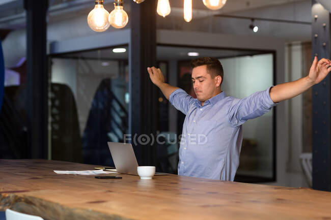 Homme d'affaires caucasien occasionnel assis au bureau et étirant. homme d'affaires au travail dans un bureau moderne. — Photo de stock