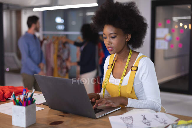 American woman fashion designer wearing tailor's tape measure using laptop thinking. independent creative design business. — Stock Photo