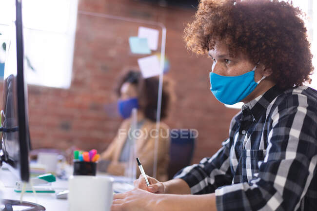 Uomo d'affari misto che indossa una maschera usando il computer in ufficio. business indipendente di design creativo durante covid 19 pandemia coronavirus. — Foto stock