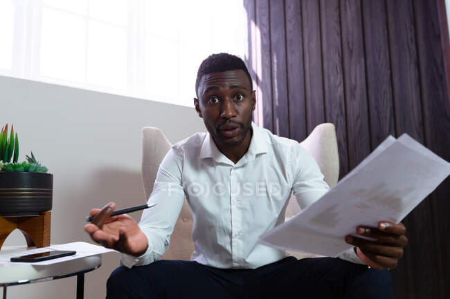 Casual african american businessman holding pen and document talking sitting in armchair. business person at work in modern office. — Stock Photo