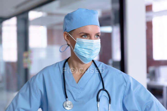 Caucasian female doctor wearing face mask, scrubs and stethoscope looking away. medical professional at work during coronavirus covid 19 pandemic. — Stock Photo