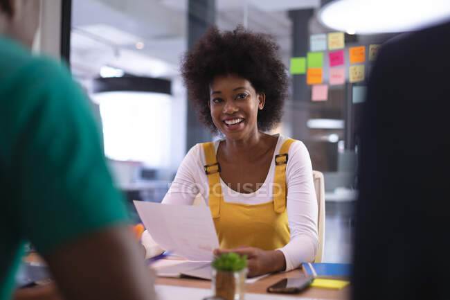 Heureuse femme afro-américaine tenant un document parlant à ses collègues dans la salle de réunion. entreprise indépendante de design créatif. — Photo de stock