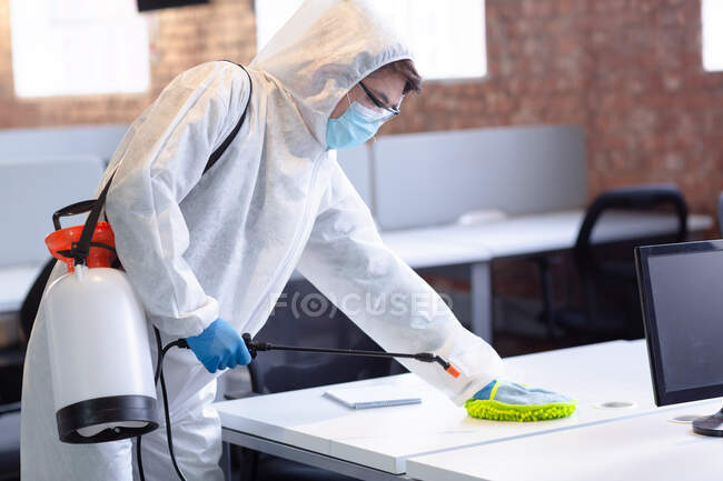 Чистіше одягайте гігієнічні комбінезони, рукавички та маску обличчя, що дезінфікує офіс та меблі. Гігієна робочого місця під час коронавірусної ковини 19 пандемії. — стокове фото