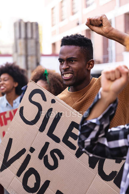 Hombre afroamericano con manifestantes en marcha sosteniendo pancartas y levantando puños. marcha por la igualdad de derechos y justicia. - foto de stock