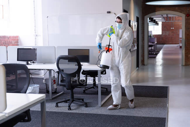 Cleaner wearing hygiene overalls, gloves and face mask carrying disinfectant in office. business workplace hygiene during coronavirus covid 19 pandemic. — Stock Photo