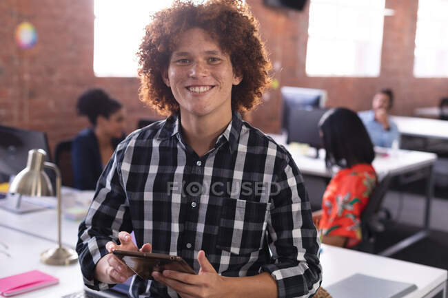 Портрет бизнесмена смешанной расы в офисе, смотрящего в камеру с помощью планшета, улыбающегося. независимый бизнес креативного дизайна. — стоковое фото