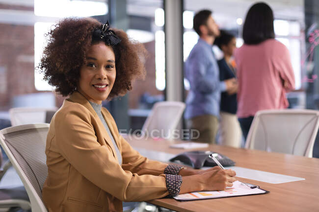 Portrait of african american buisnesswoman sitting at desk with documents looking to camera. independent creative design business. — Stock Photo