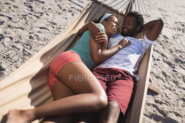 Feliz casal afro-americano deitado em rede na praia abraçando. tempo de lazer ao ar livre saudável pelo mar. — Fotografia de Stock