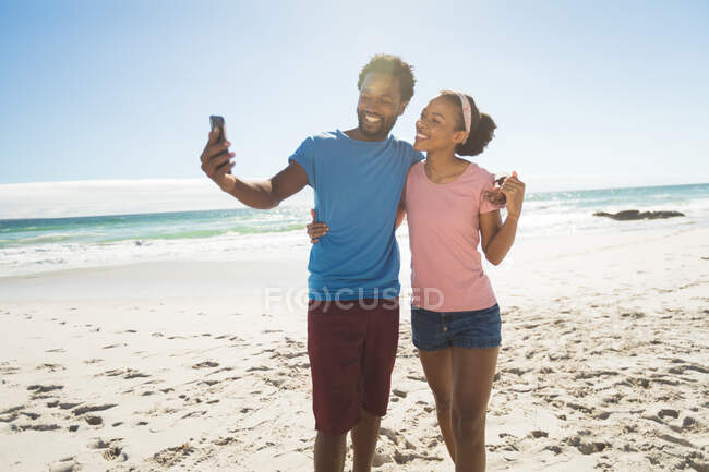 Счастливая африканская американская пара на пляже у моря делает селфи. здоровый отдых на открытом воздухе у моря. — стоковое фото