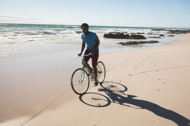 Homem americano africano feliz na praia andar de bicicleta. tempo de lazer ao ar livre saudável pelo mar. — Fotografia de Stock