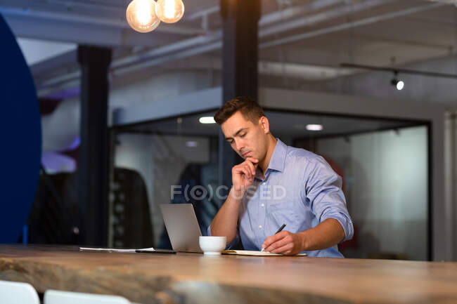 Lässiger kaukasischer Geschäftsmann sitzt am Schreibtisch, denkt nach und schreibt Notizen. Geschäftsmann bei der Arbeit im modernen Büro. — Stockfoto