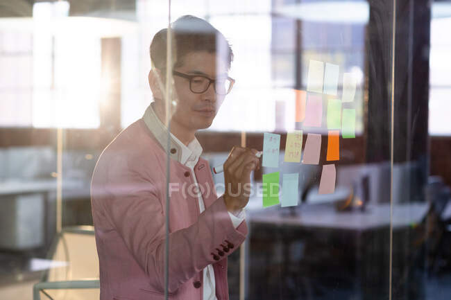 Elegante hombre de negocios asiático escribiendo notas en la pared de cristal. persona de negocios en el trabajo en la oficina moderna. - foto de stock