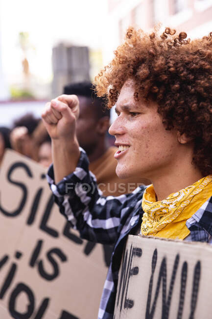 Hombre de raza mixta gritando con manifestantes en marcha sosteniendo carteles y levantando puños. marcha por la igualdad de derechos y justicia. - foto de stock