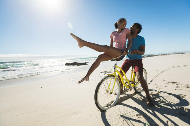 Happy african american couple riding bicycle on the beach. healthy outdoor leisure time by the sea. — Stock Photo