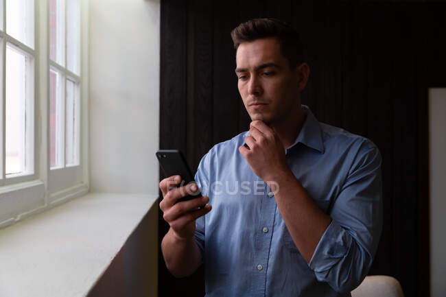 Portrait of stylish caucasian businessman thinking and using smartphone. business person at work in modern office. — Stock Photo