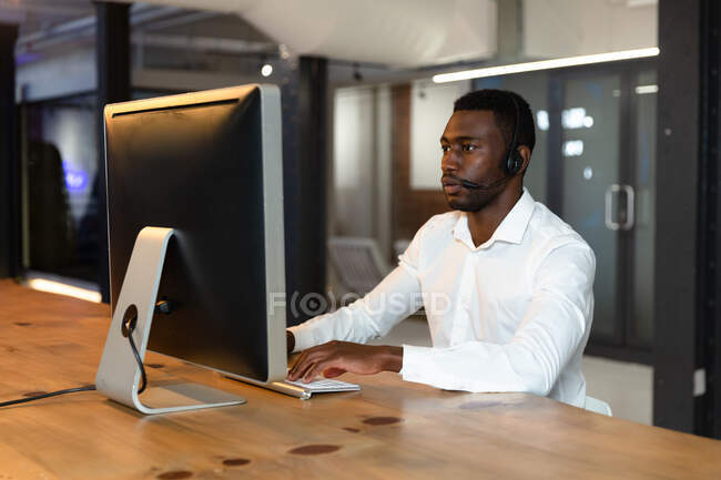 Афроамериканський бізнесмен, який сидить за столом, користується комп 
