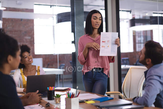 Mixed race businesswoman speaking to diverse group of colleagues in meeting room holding document. independent creative design business. — Stock Photo