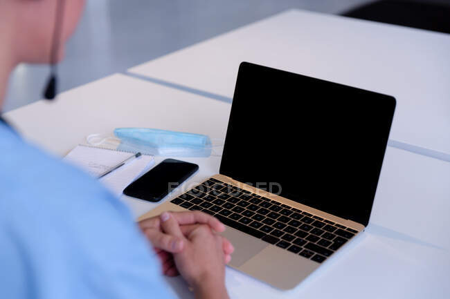 Над видом на плече кавказької жінки-лікар за столом, використовуючи ноутбук під час консультації з відеодзвінками. телемедицина під час карантину . — стокове фото
