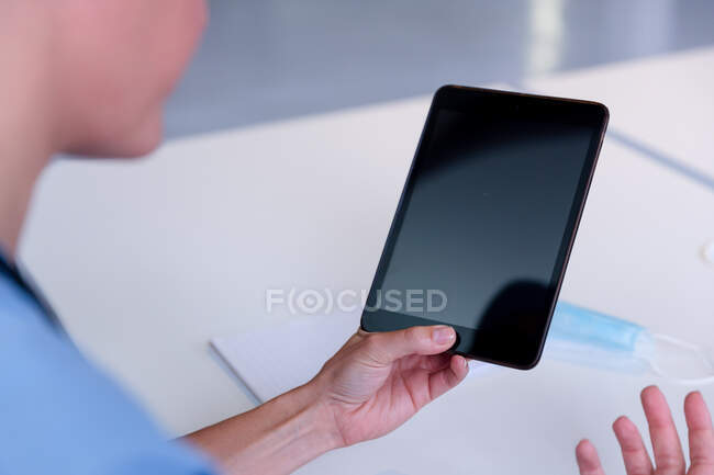 Over shoulder view of caucasian female doctor at desk using tablet for video call consultation. telemedicine during quarantine lockdown. — Stock Photo