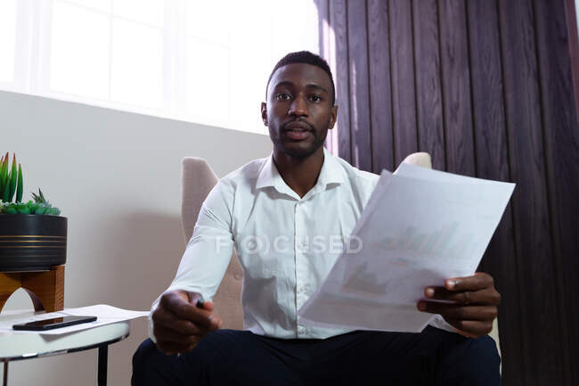 Retrato de empresário americano africano casual segurando documento sentado em poltrona. pessoa de negócios no trabalho em escritório moderno. — Fotografia de Stock