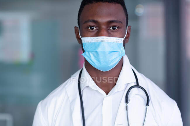 Porträt eines afrikanisch-amerikanischen Arztes mit Mundschutz, weißem Mantel und Stethoskop. Mediziner bei der Arbeit während Coronavirus covid 19 Pandemie. — Stockfoto