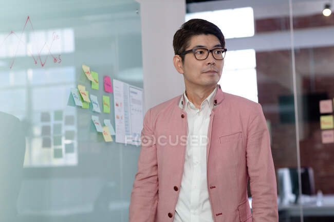 Porträt eines stilvollen asiatischen Geschäftsmannes an einer Glaswand, der wegschaut. Geschäftsmann bei der Arbeit im modernen Büro. — Stockfoto