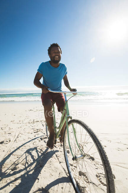 Heureux homme afro-américain sur la plage à vélo. loisirs en plein air sains au bord de la mer. — Photo de stock