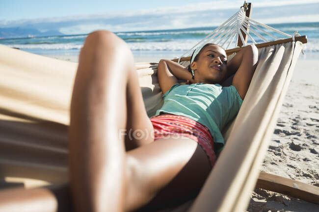 Happy african american woman laying in hammock on the beach. healthy outdoor leisure time by the sea. — Stock Photo