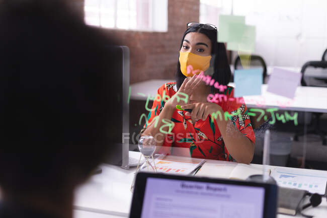 Mixed rase businesswoman wearing mask pointing at glass wall. independent creative design business during covid 19 coronavirus pandemic. — Stock Photo