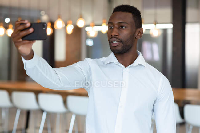 Casual empresário afro-americano tomando selfie e usando smartphone. pessoa de negócios no trabalho em escritório moderno. — Fotografia de Stock