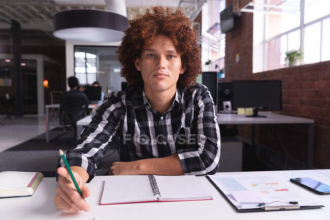 Портрет бізнесмена змішаної раси в офісі сидить, тримаючи олівець, дивлячись на камеру. Незалежний творчий бізнес. — стокове фото