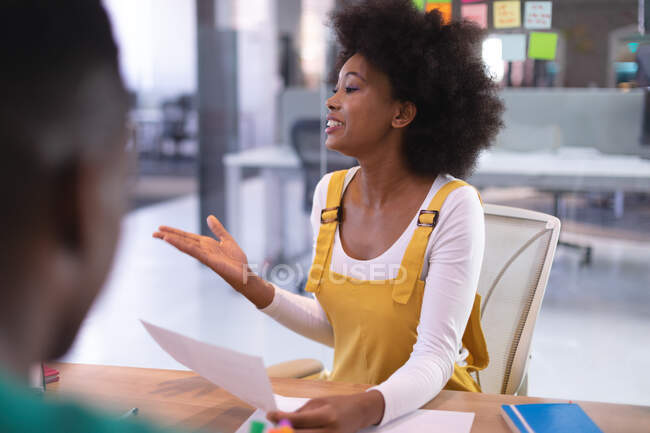 Glückliche afrikanisch-amerikanische Geschäftsfrau hält Dokument in der Hand und spricht mit Kollegen im Besprechungsraum. unabhängiges kreatives Designgeschäft. — Stockfoto