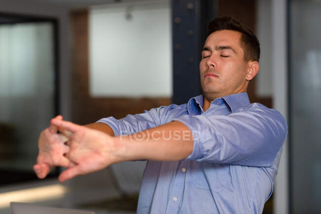 Casual caucasian businessman sitting at desk and stretching with eyes closed. business person at work in modern office. — Stock Photo