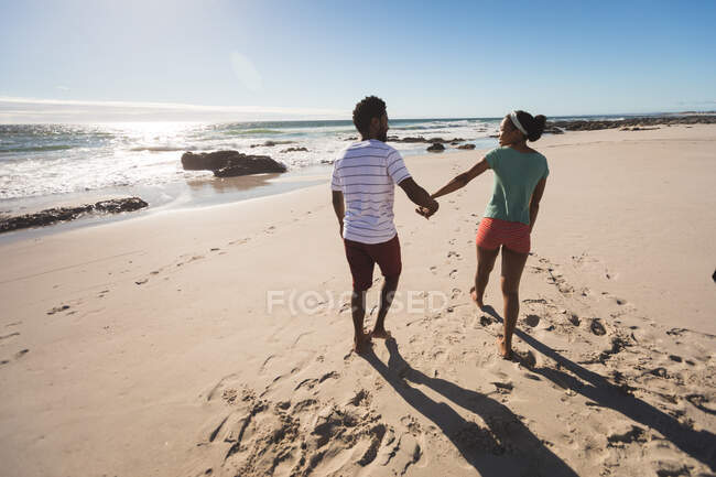 Африканская американская пара, идущая по пляжу, держась за руки. здоровый отдых на открытом воздухе у моря. — стоковое фото