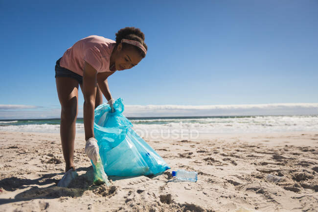 Donna afroamericana che indossa guanti di lattice raccogliendo spazzatura dalla spiaggia. eco estate spiaggia conservazione — Foto stock