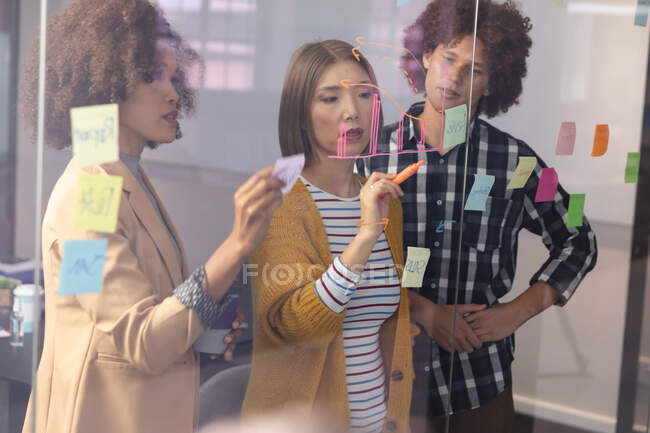 Diverse group of creative colleagues brainstorming writing notes on glass wall in meeting room. independent creative design business — Stock Photo