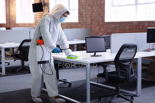 Чистильщик в гигиеническом комбинезоне, перчатках и маске для дезинфекции офиса и мебели. гигиена рабочего места во время пандемии коронавируса. — стоковое фото
