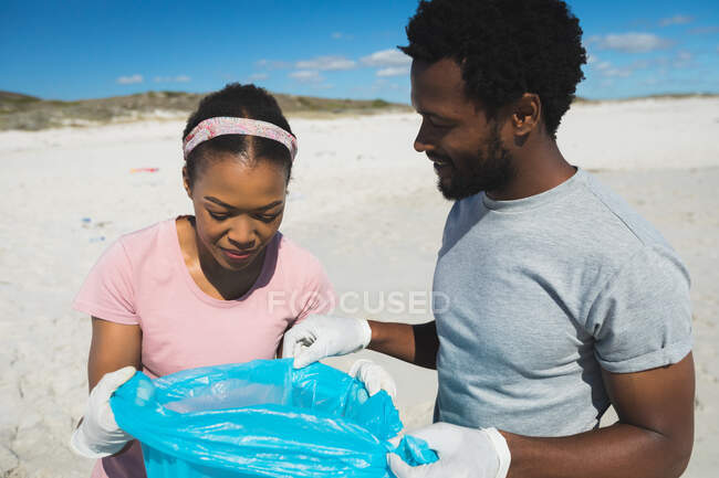 Африканская американская пара в латексных перчатках собирает мусор с пляжа. Охрана экологического пляжа — стоковое фото