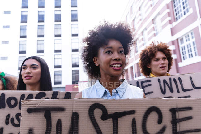 Drei unterschiedliche männliche und weibliche Demonstranten auf dem Marsch halten selbstgebastelte Protestschilder hoch und lächeln. Demonstrationszug für Gleichberechtigung und Gerechtigkeit. — Stockfoto