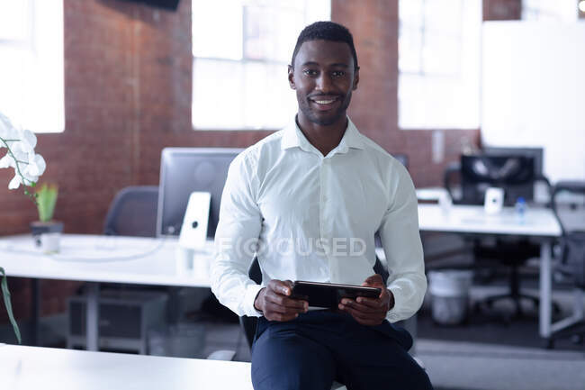 Портрет звичайного афроамериканського бізнесмена, який сидить на столі з планшетом. Бізнесмен на роботі в сучасному офісі.. — стокове фото