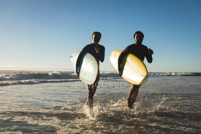 Щаслива афро-американська пара біжить по морю з дошками для серфінгу. Здоровий вільний час на відкритому повітрі біля моря. — стокове фото