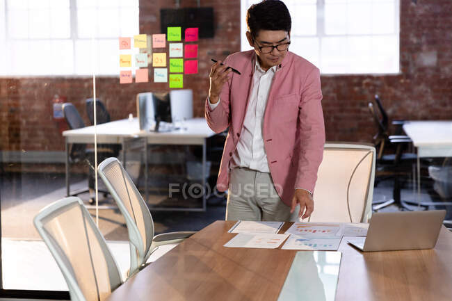Стильний азіатський бізнесмен, який розмовляє стоячи за столом, використовує смартфон. бізнесмен на роботі в сучасному офісі . — стокове фото